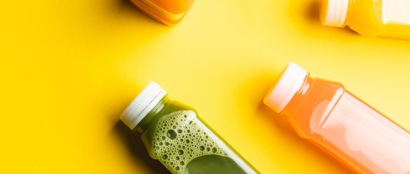 Zumos de colores en botellas de plástico sobre fondo amarillo.