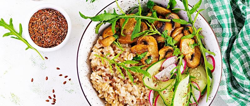 Gachas de avena para el desayuno con hierbas verdes sobre champiñones, pepino, rábano y semillas de lino.