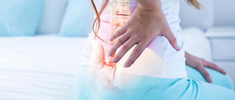 Figura femenina de espaldas en la cama sobre fondo minimalista pálido. Gráfico superpuesto de la columna vertebral y la pelvis.
