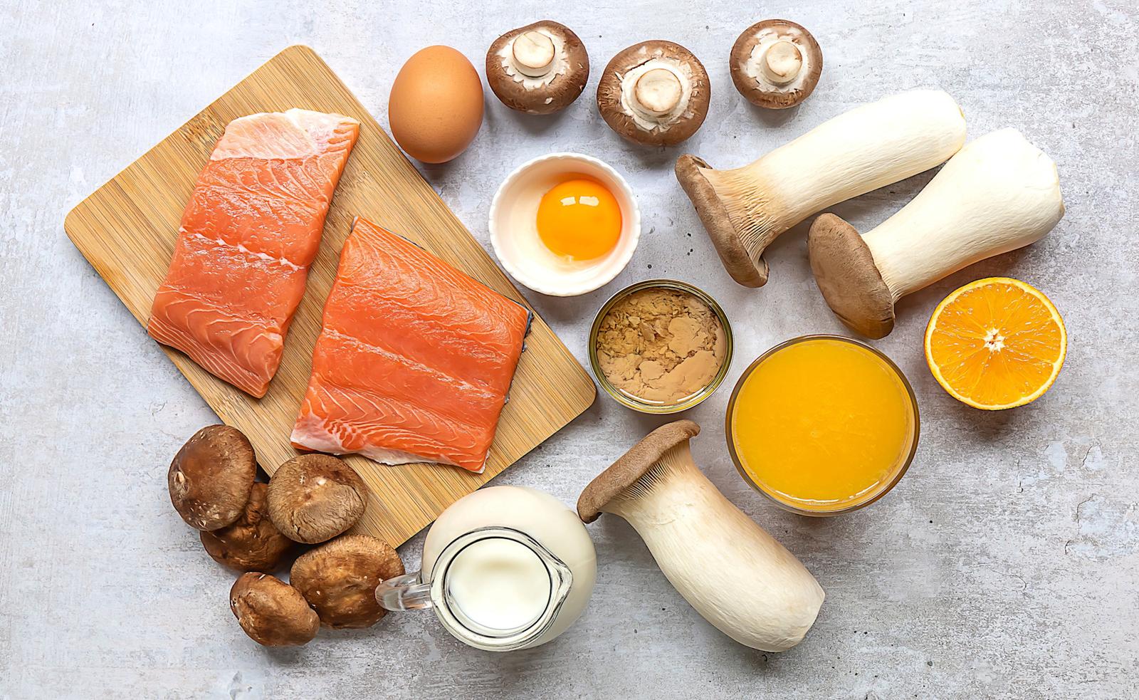 A selection of foods high in vitamin d that includes salmon, mushroom, egg yolk, and oranges.