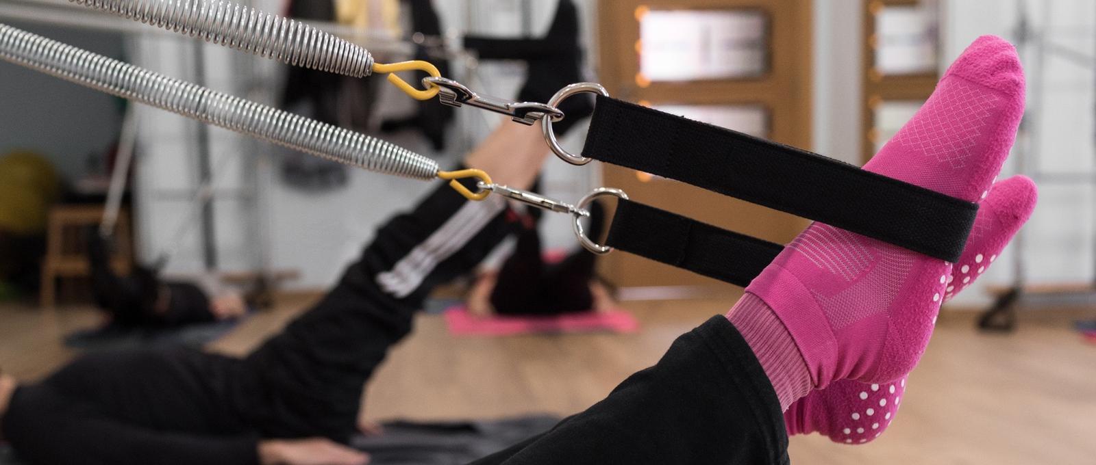 Mujer anónima con calcetines brillantes levantando las piernas y estirando los muelles durante un entrenamiento de Pilates en grupo en un estudio