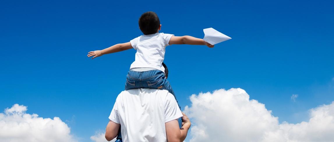 Hijo sentado en el hombro de su padre y lanzando un avión de papel