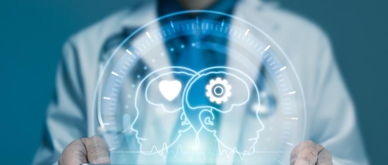 Profesional médico sosteniendo holograma digital que muestra dos cabezas de perfil con símbolos de corazón y engranaje que representan tecnología sanitaria.