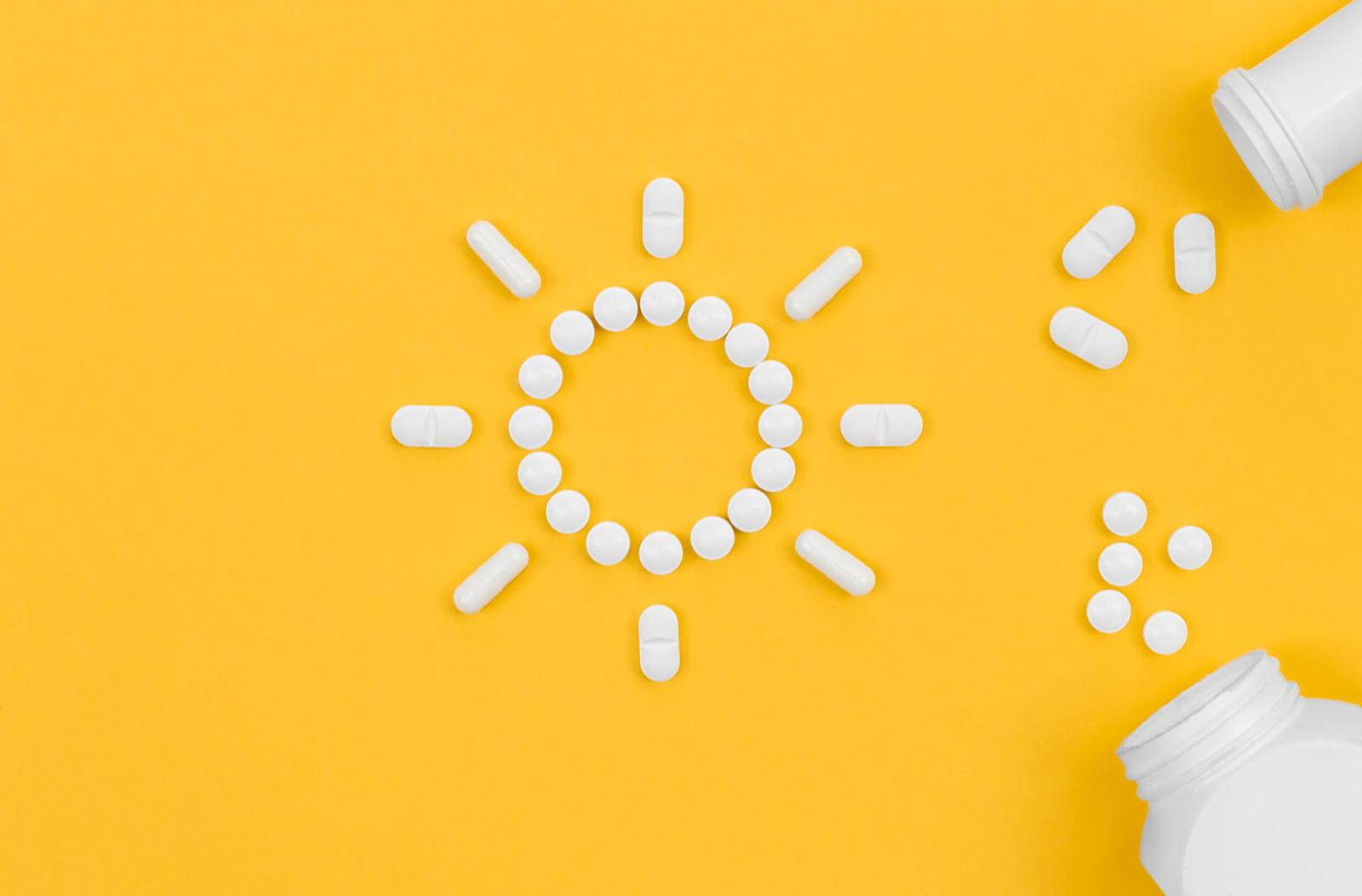 A yellow background with 2 bottles of pills spilling pills. In the middle is the shape of a sun made out of pills.