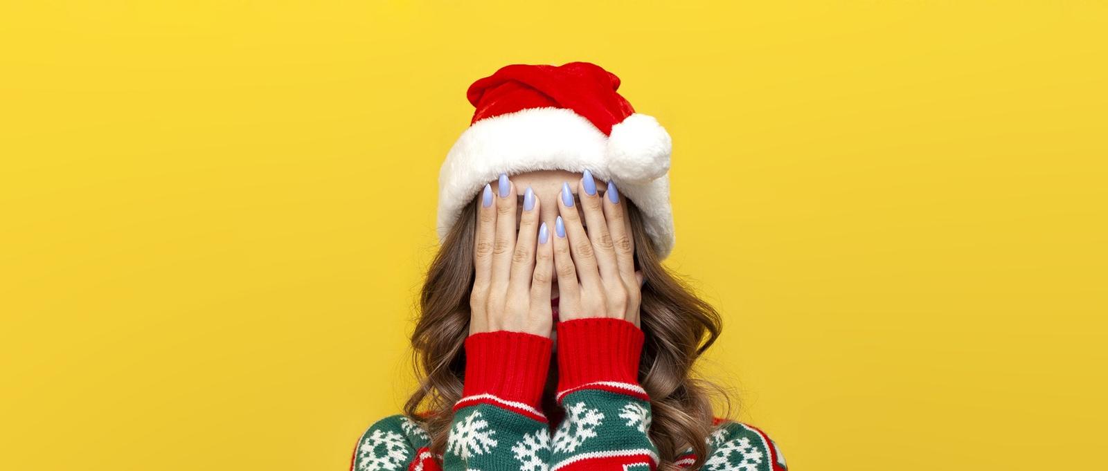 Chica en suéter de Navidad y el sombrero de Santa Claus se cubre la cara con la mano y es tímido sobre fondo amarillo aislado, la mujer oculta su rostro en el estrés y la depresión en la ropa de Año Nuevo