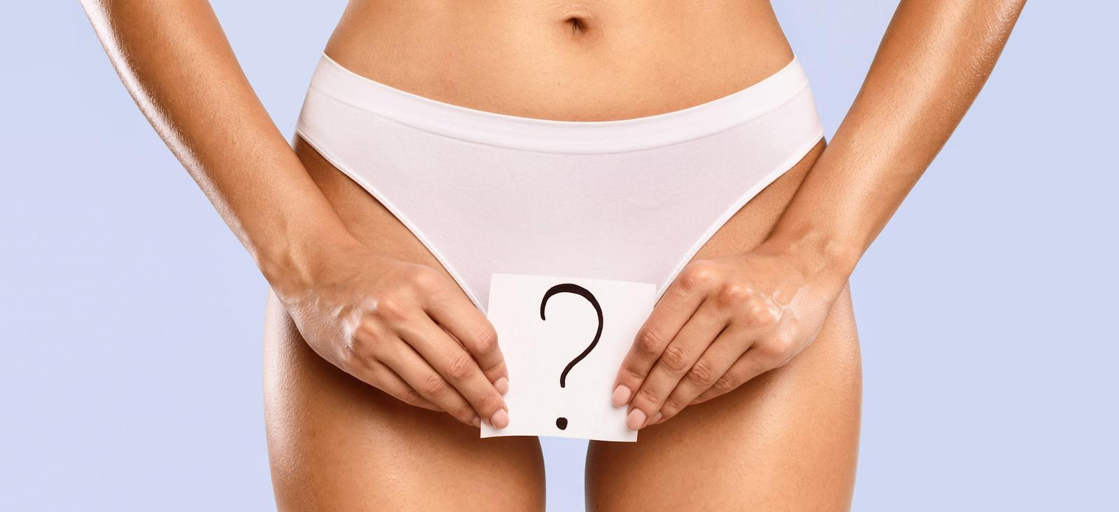 A woman holding a cardboard cutout of a question mark in front of her pubic area.