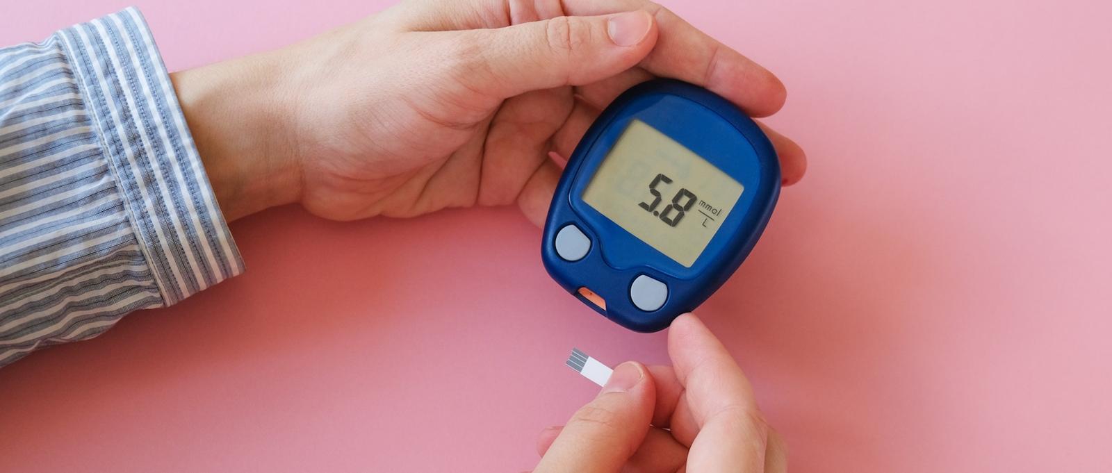 Primer plano de un par de manos sosteniendo un glucómetro.