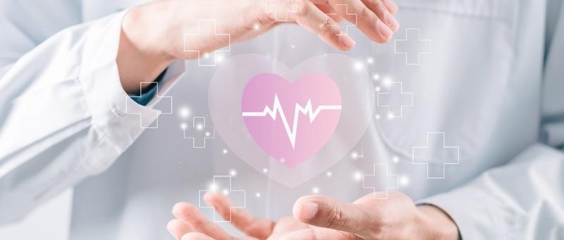 Manos de profesional sanitario rodeando un corazón digital rosa con línea de latido, rodeado de símbolos médicos en forma de cruz.