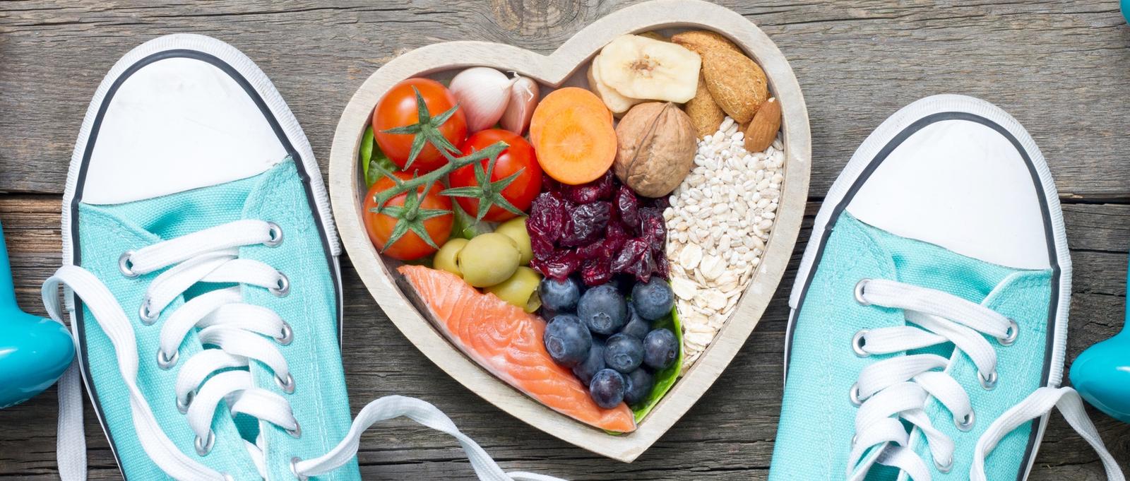 Concepto de estilo de vida saludable con alimentos en el corazón y accesorios deportivos de fitness en tablas de madera.