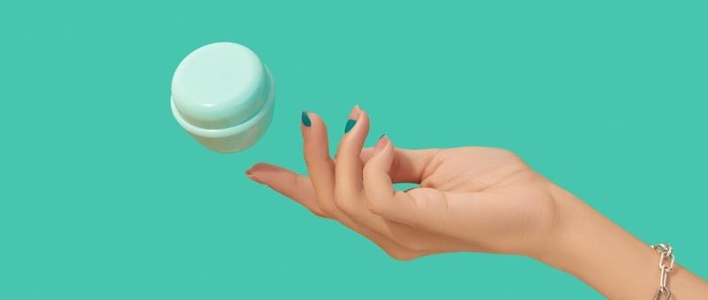 Female hand holding white jar on turquoise background.