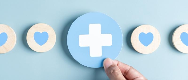 Mano sosteniendo farmacia blanca y azul cruz entre corazones azules y blancos sobre fondo azul.