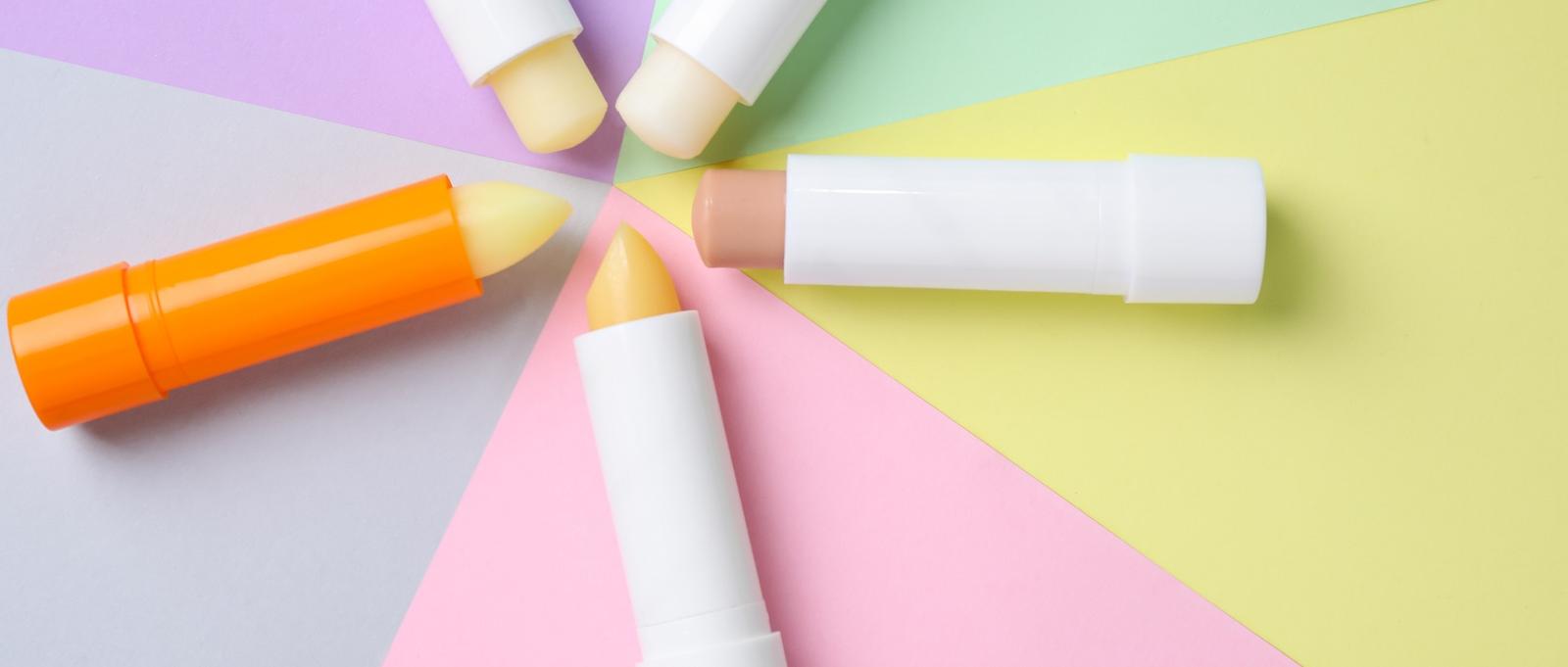 Coloridos bálsamos labiales dispuestos en círculo sobre secciones de fondo pastel de color morado, rosa, amarillo y verde.