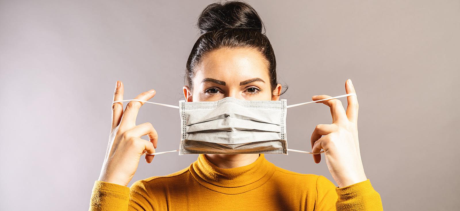 A woman holding a mask over her face.