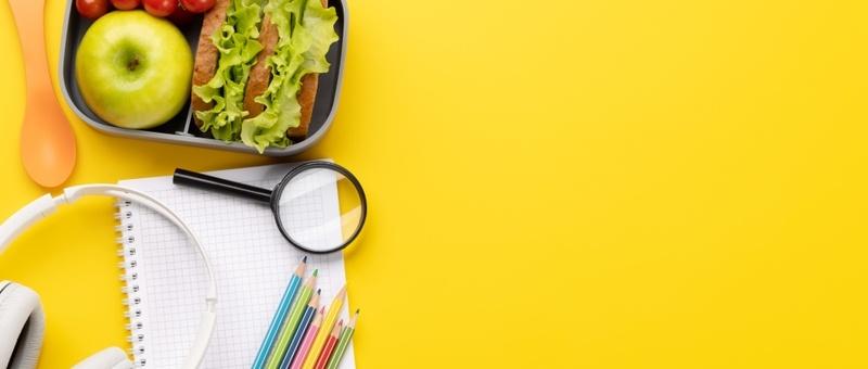 Almuerzo con útiles de estudio sobre fondo amarillo.