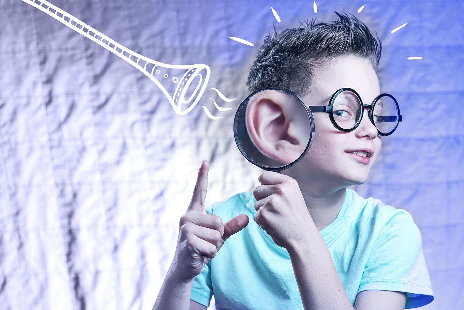 Niño con gafas redondas y lupa en la oreja, con ondas sonoras de trompeta ilustradas cerca.