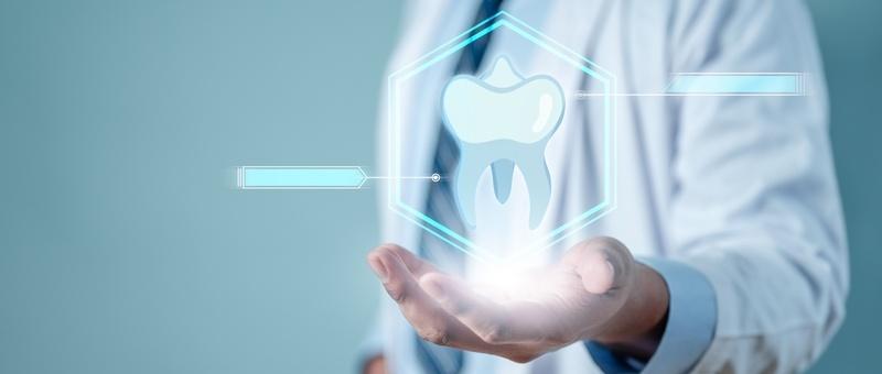 Profesional de la odontología sosteniendo un holograma digital de un diente, que representa la tecnología dental moderna sobre fondo verde azulado.