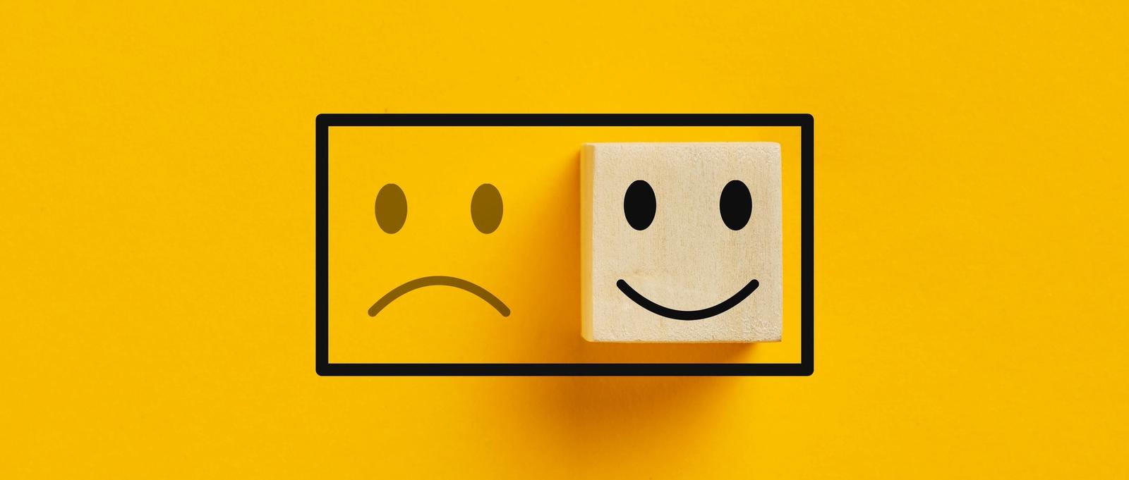 Dos cubos de madera con icono de estado de ánimo feliz sobre icono de estado de ánimo triste sobre fondo amarillo