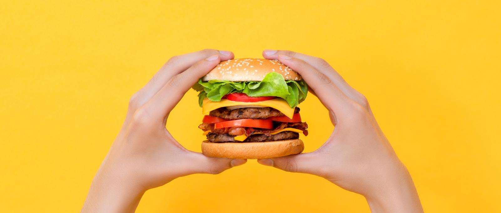 Manos sosteniendo hamburguesa sobre fondo amarillo aislado