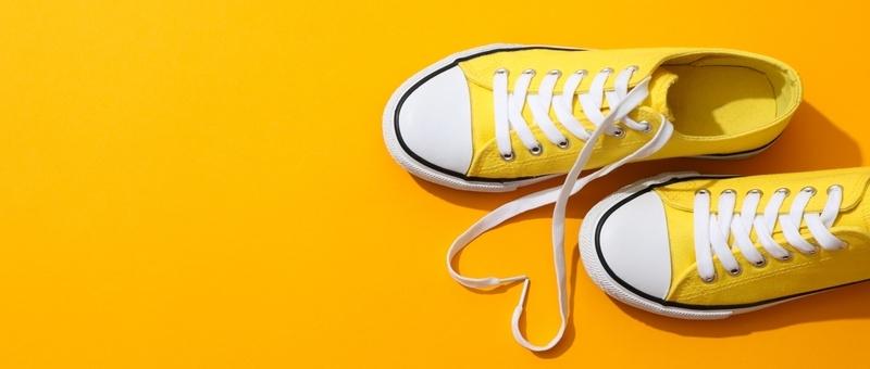 Pair of yellow and white walking shoes - Converse style - against a yellow background.