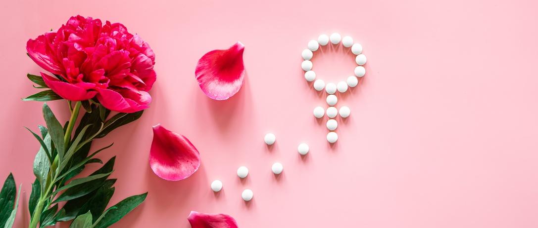 Género Venus símbolo hecho de píldoras, y pétalos de flores de peonía sobre un fondo de color rosa, período de la mujer y el concepto de salud.