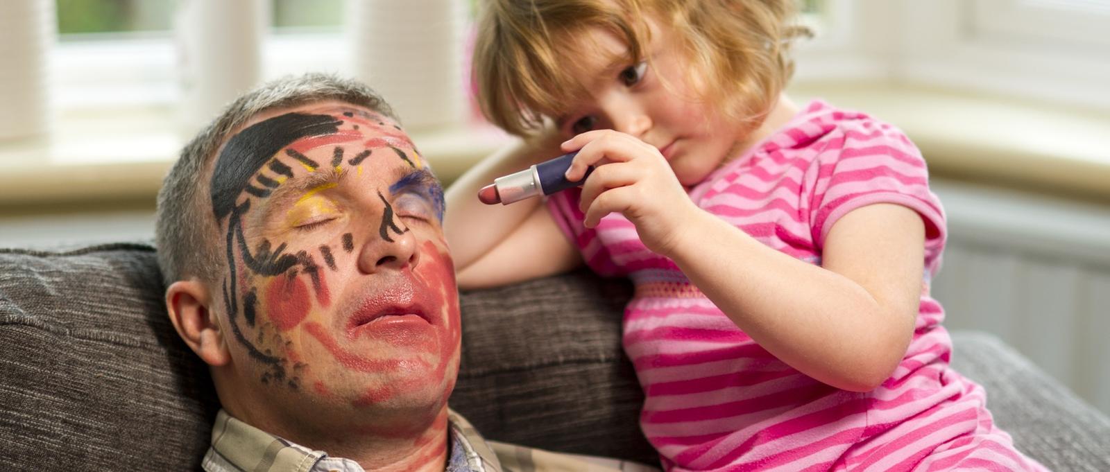 Niña dibujando en la cara de su padre dormido