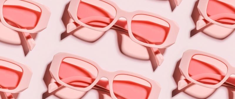 Multiple pairs of pink sunglasses with rose-tinted lenses arranged in a pattern on a light background.