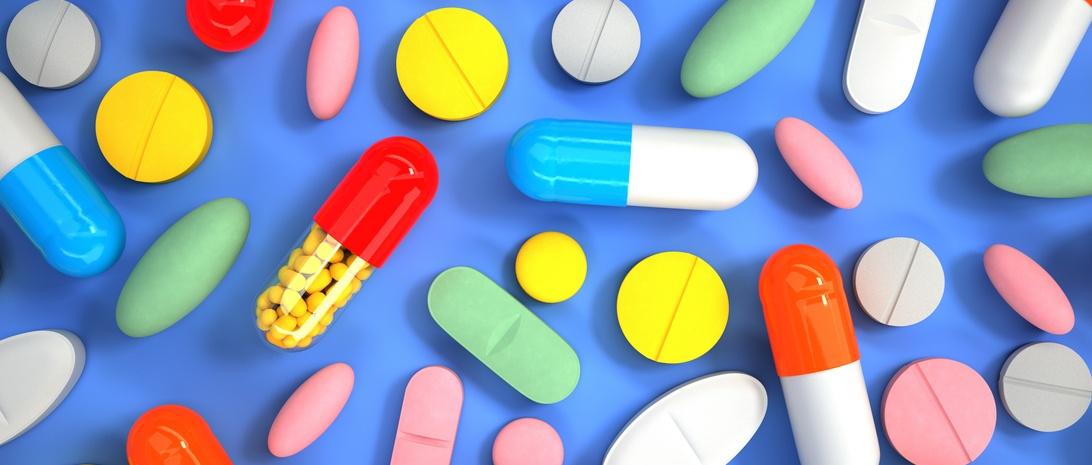 Colorido surtido de píldoras, pastillas y cápsulas esparcidas sobre fondo azul, incluyendo medicamentos rojos, amarillos, azules y verdes.
