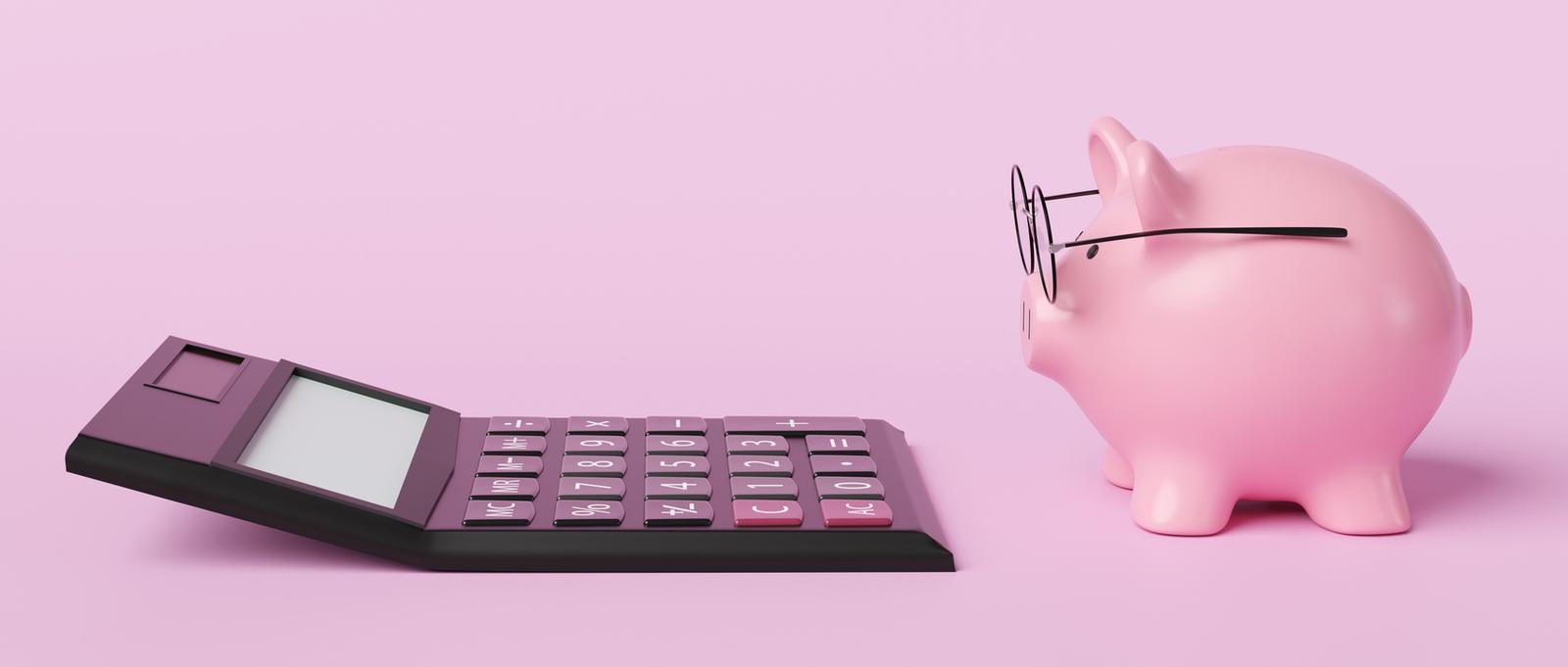 Hucha rosa con gafas delante de una calculadora negra sobre fondo rosa.