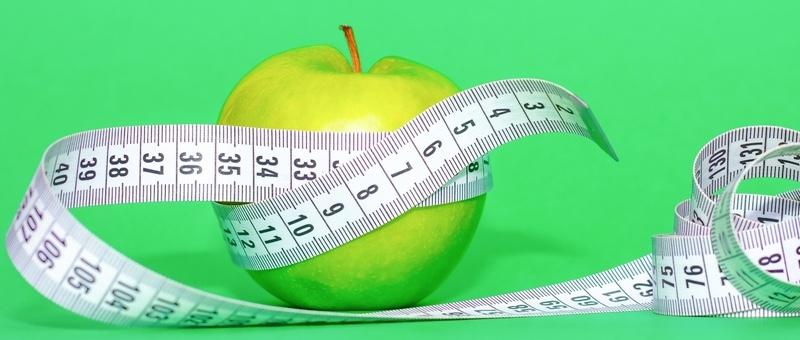 Manzana verde envuelta en cinta métrica sobre fondo verde.