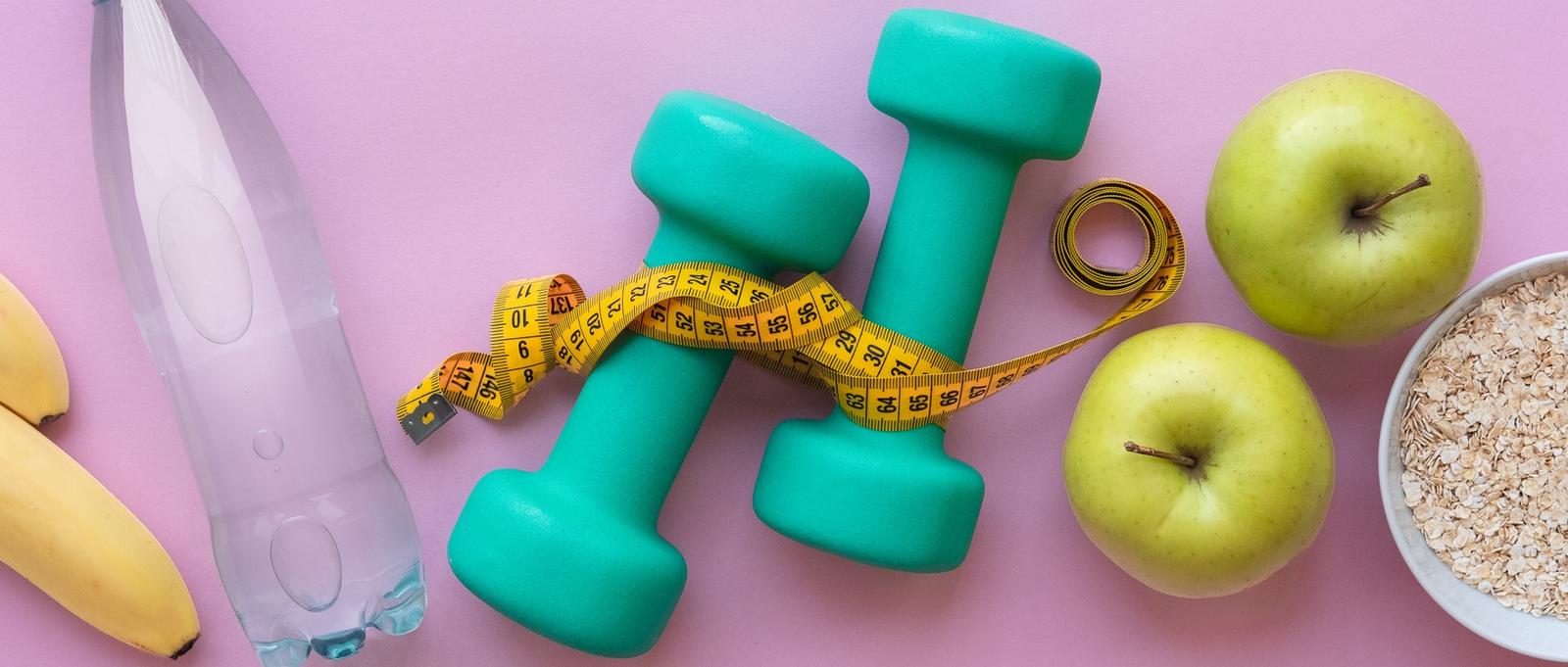 Concepto de fitness - manzanas, agua, mancuernas y cuerda de saltar sobre fondo rosa