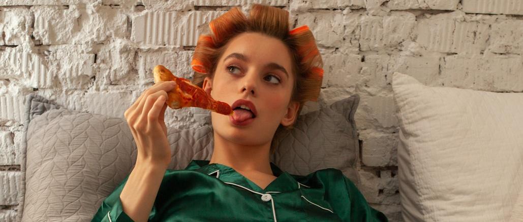 joven mujer de moda en pijama con caja de pizza en la cama en casa