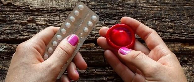 Una mujer sostiene la píldora anticonceptiva y un preservativo rojo