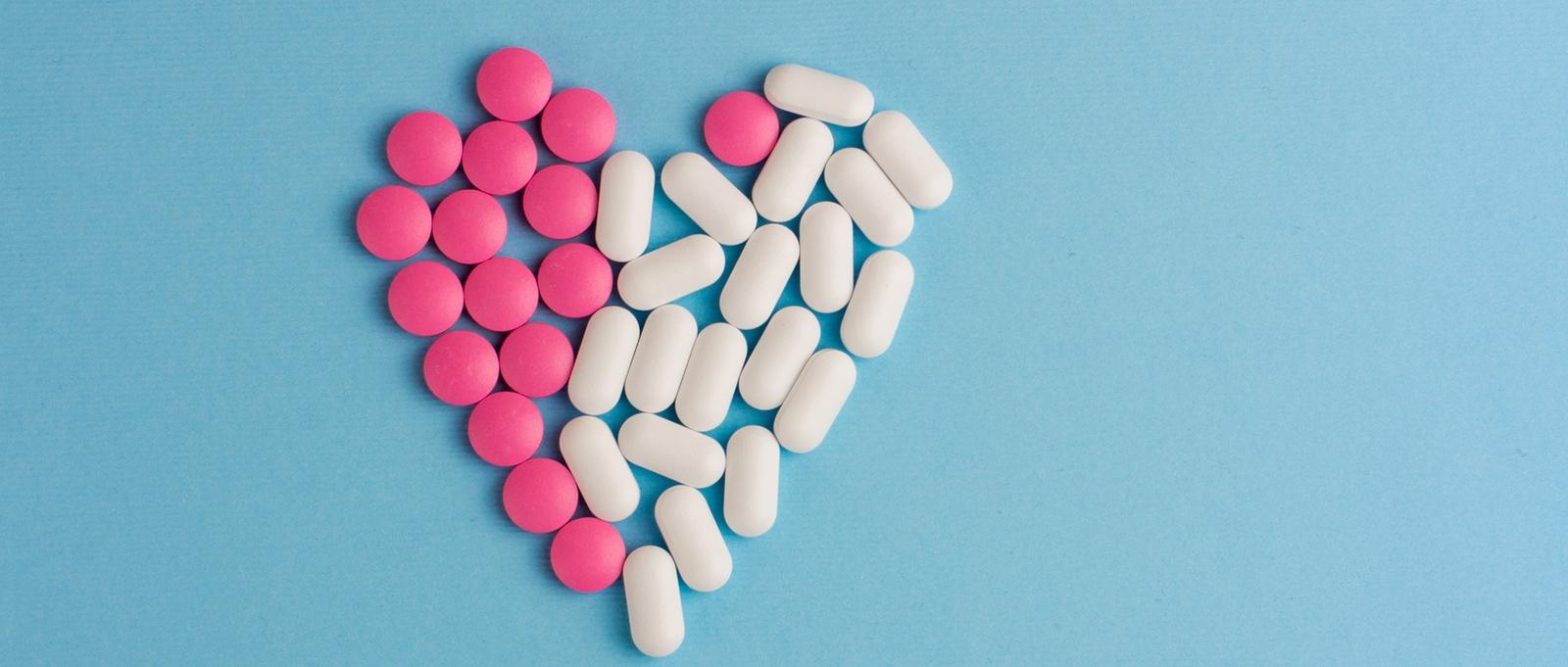 Píldoras rosas y blancas en forma de corazón sobre fondo azul