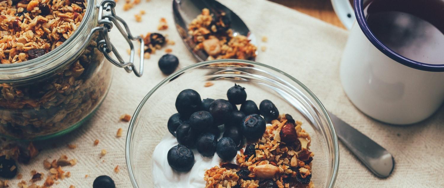 Arándanos frescos y granola casera en un bol de cristal con yogur, junto a un tarro de granola.