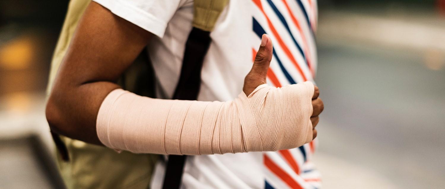 Persona con camisa blanca a rayas rojas y azules que muestra una mano y un antebrazo envueltos en un vendaje beige.
