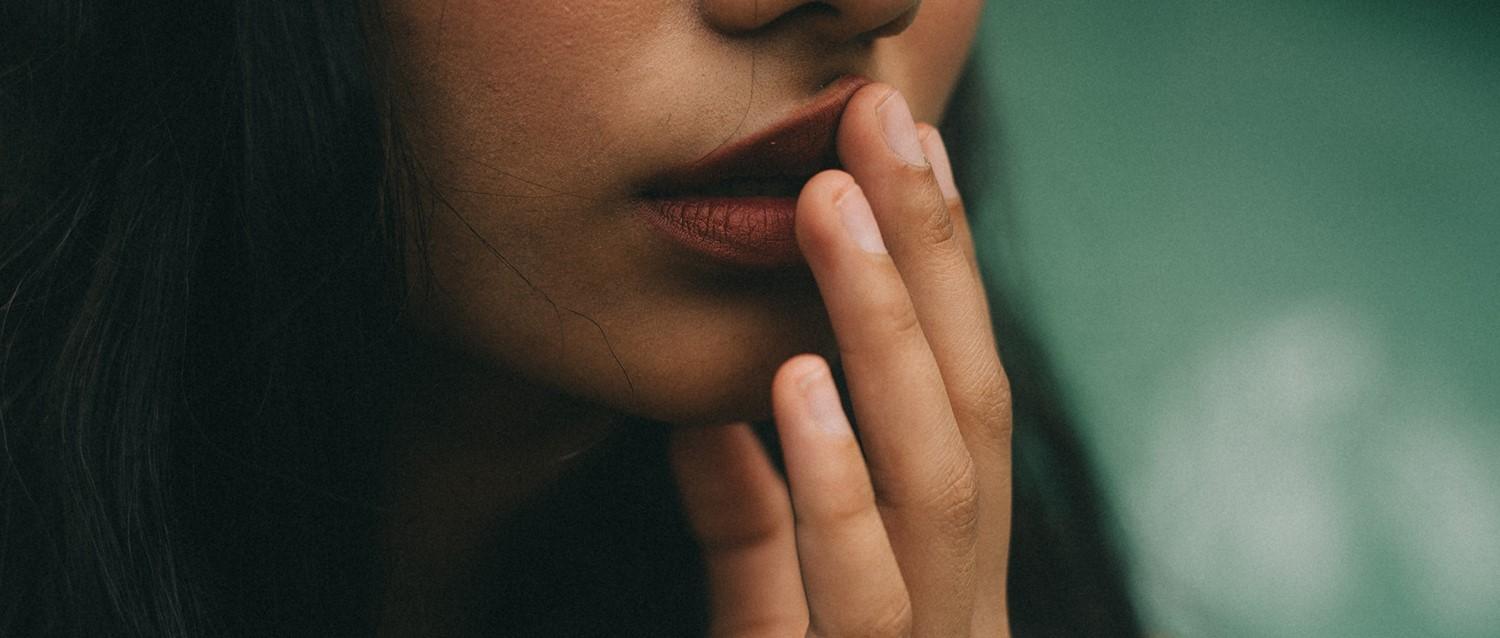 Primer plano de una persona con los labios rojos tocándose la cara pensativamente sobre un fondo verde suave.