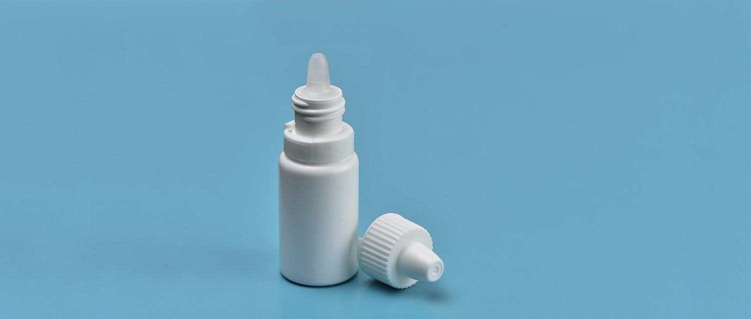 Frasco blanco de colirio o spray nasal con el tapón quitado, sobre fondo azul claro.