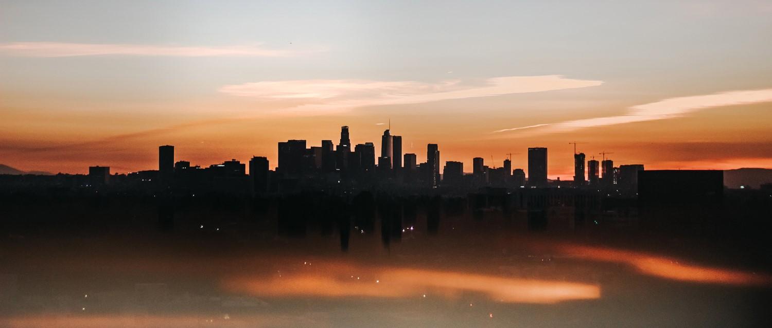 La silueta del horizonte de Los Ángeles sobre un espectacular cielo anaranjado al atardecer, con los rascacielos reflejados en el agua.