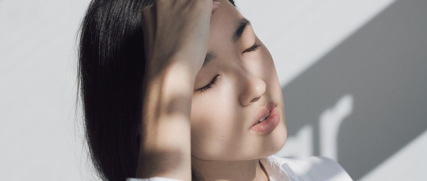 Persona con el pelo oscuro y los ojos cerrados en una iluminación suave, con sombras que crean un ambiente sereno y tranquilo.
