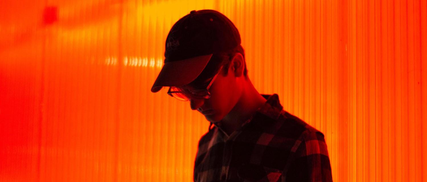 Silueta de persona con gorra y gafas sobre fondo naranja vibrante con rayas verticales de luz.