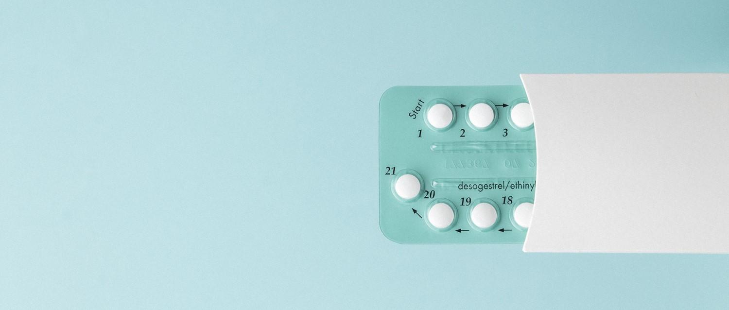 Paquete de píldoras anticonceptivas que muestra comprimidos blancos numerados en un blíster verde azulado sobre un fondo azul claro.