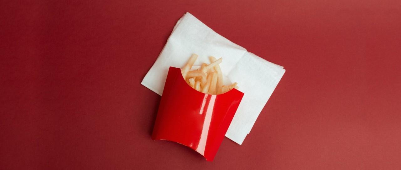 Patatas fritas en un recipiente de cartón rojo sobre una servilleta blanca y fondo rojo.