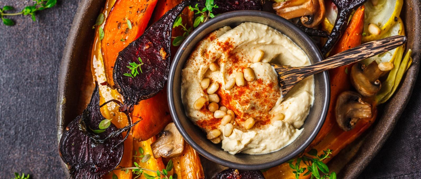 Zanahorias, remolachas, calabacines y boniatos al horno con hummus en un plato oscuro.