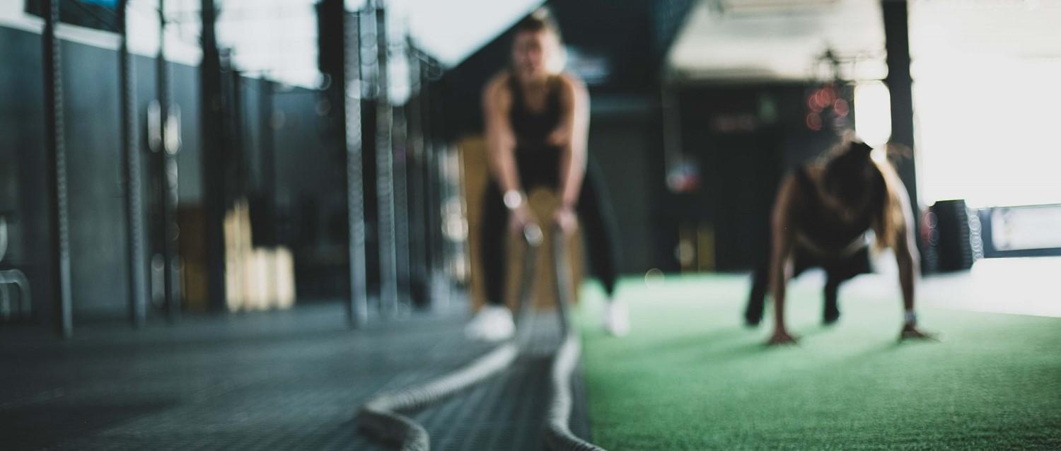 Figuras borrosas haciendo ejercicio en un gimnasio moderno con suelo verde, centrándose en el entrenamiento de fuerza en un entorno oscuro.